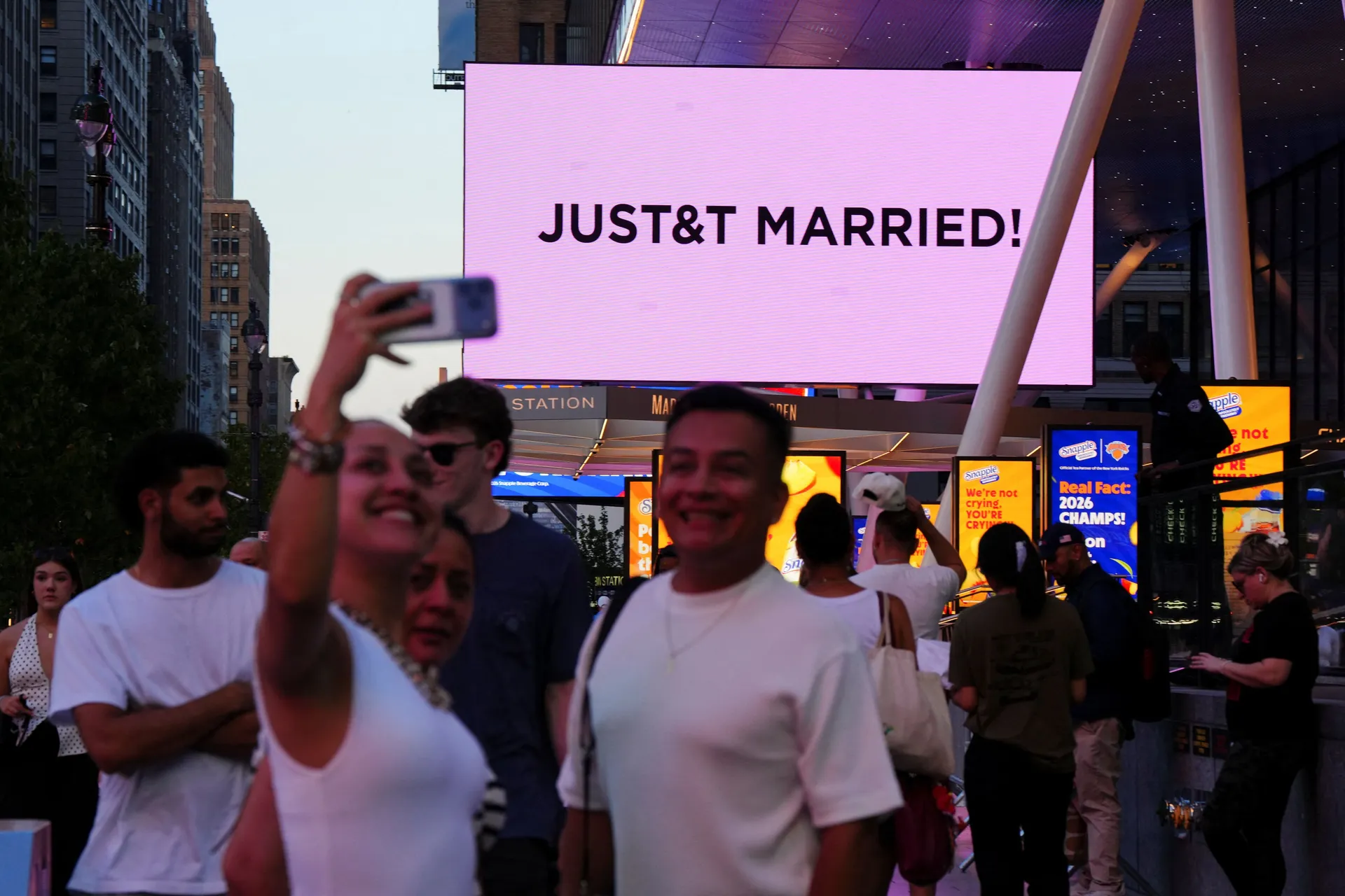People take selfies next to a screen displays a message referencing singer Taylor Swift and National Football League (NFL) player Travis Kelce outside Madison Square Garden, the venue for their wedding celebrations, in New York, U.S., July 3, 2026.  REUTE