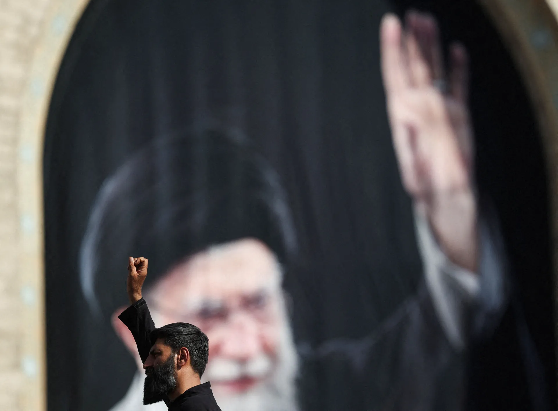 A man raises his hand with a banner of late Supreme Leader Ayatollah Ali Khamenei in the background on the day of a public farewell ceremony to pay their respects to Khamenei, who was killed on February 28 in Israeli and U.S. airstrikes, at the Imam Khome
