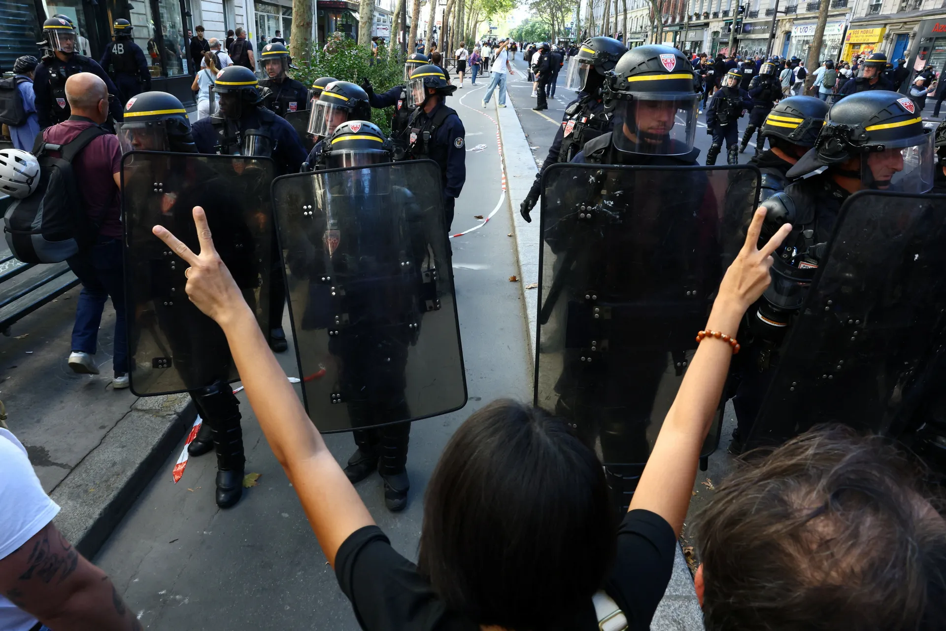 A protester makes the V-for-victory sign towards French CRS riot police who stand in position amid clashes during a demonstration by high school and university students, supported by teachers' union and school parents, in Paris as part of a nationwide day