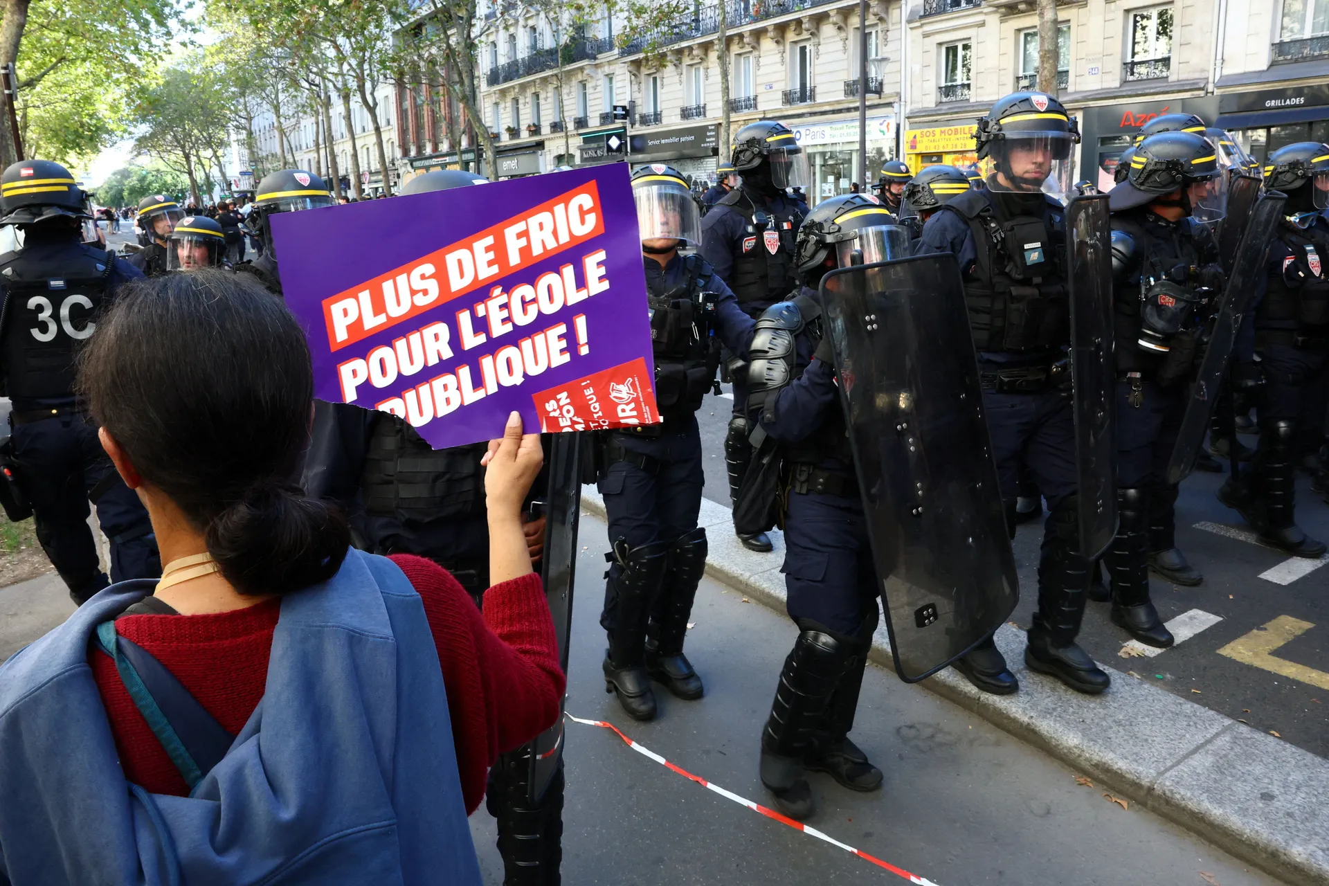 A protester holds a placard reading "More money for public schools" towards French CRS riot police who stand in position during a demonstration by high school and university students, supported by teachers' union and school parents, in Paris as part of a 