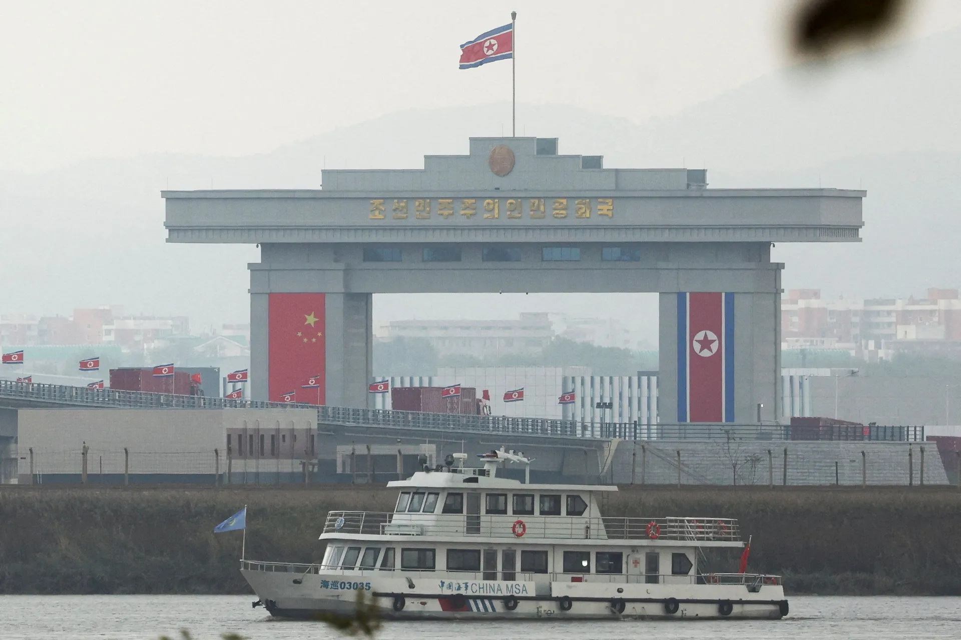 A Chinese maritime patrol vessel travels along the Yalu river as trucks adorned with Chinese flags cross the newly opened New Yalu River Bridge into North Korea's Sinuiju from China's Dandong New Zone, as seen from Dandong, Liaoning province, China Octobe