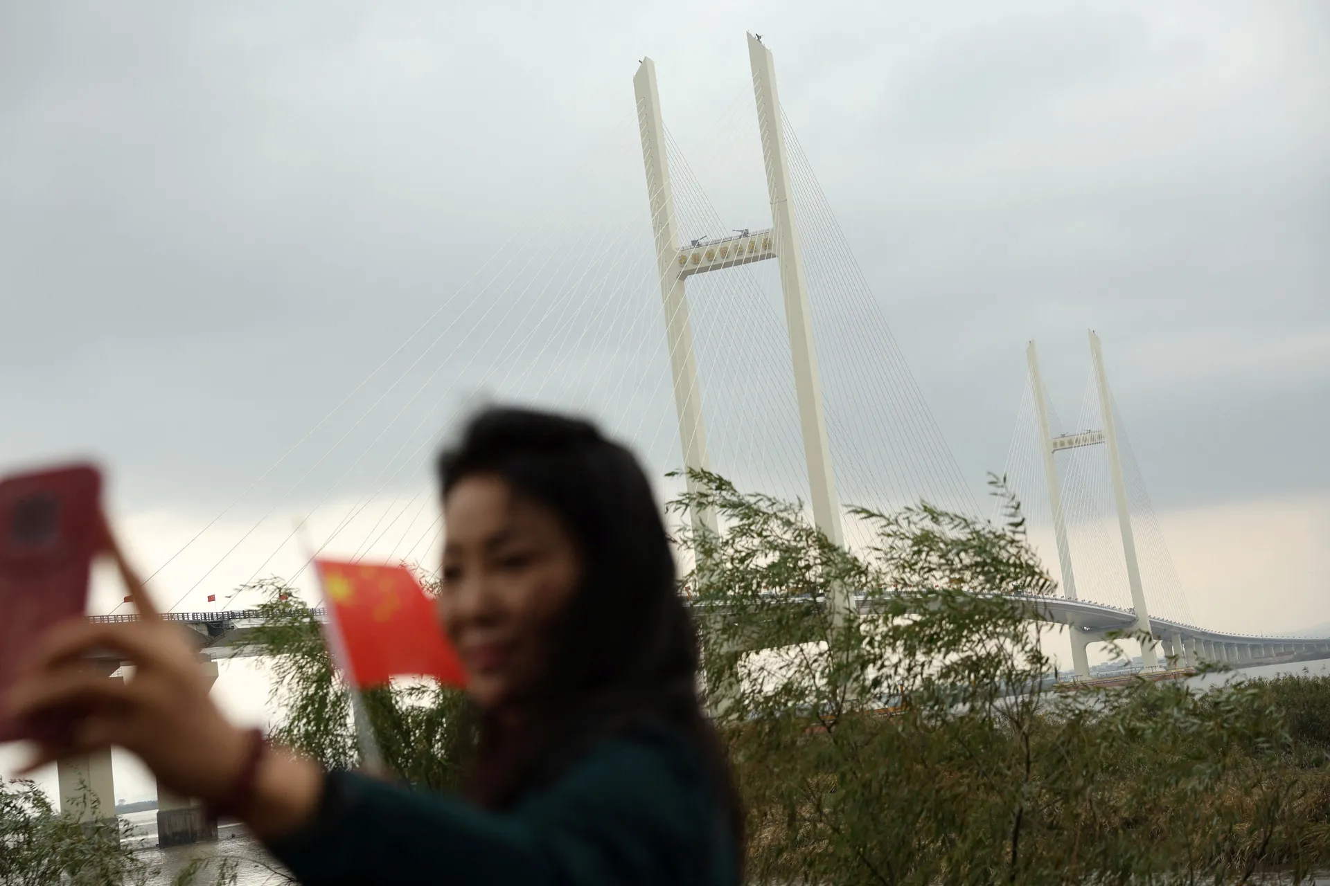 A resident poses with a Chinese flag in front of the newly opened New Yalu River Bridge, which connects China's Dandong New Zone and North Korea's Sinuiju, in Dandong, Liaoning province, China October 15, 2026. REUTERS/Florence Lo