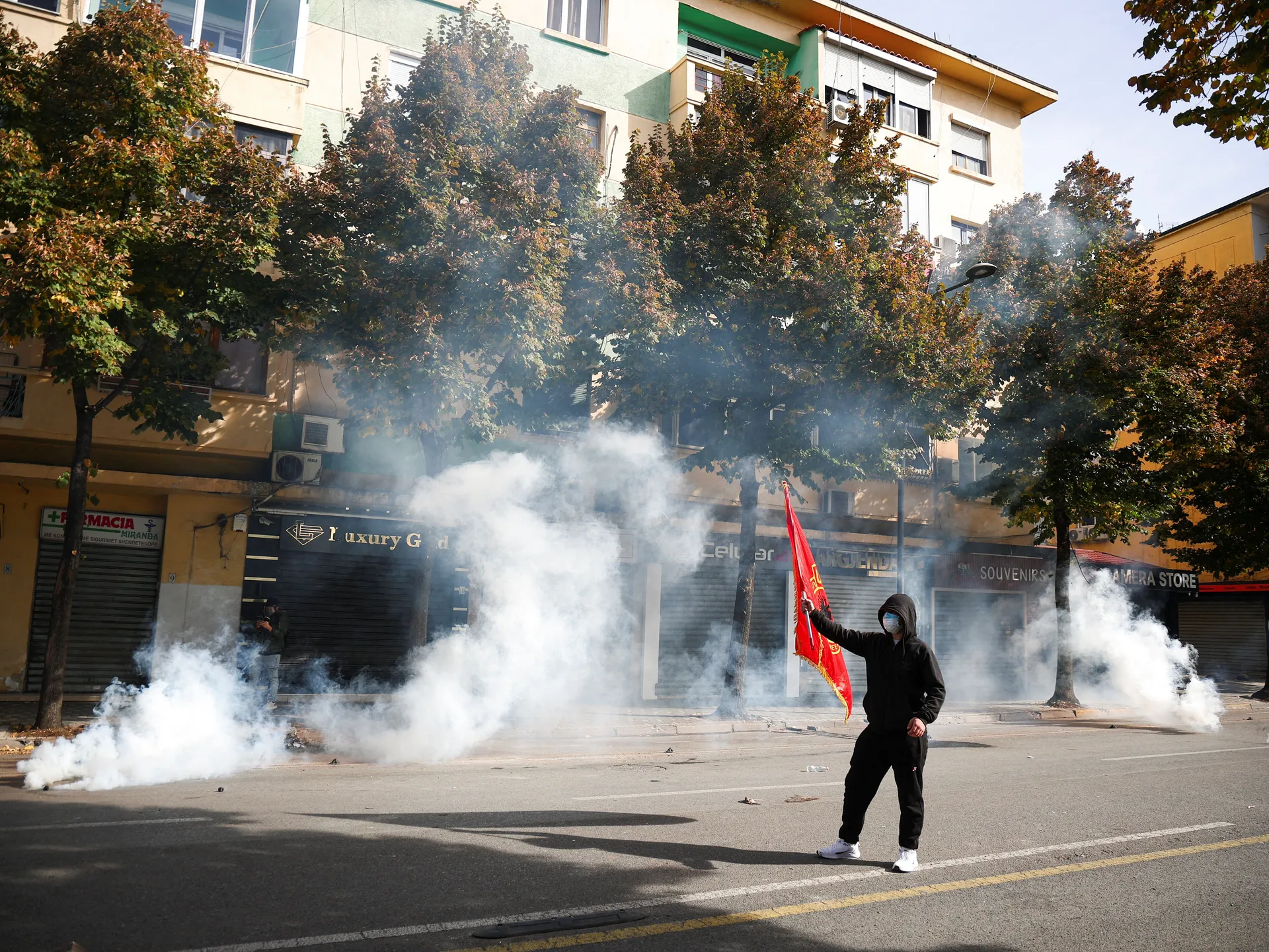 A protester stands holding a flag as smoke billows from tear-gas canisters amid an anti-government protest by students, in Tirana, Albania, October 15, 2026. REUTERS/Florion Goga