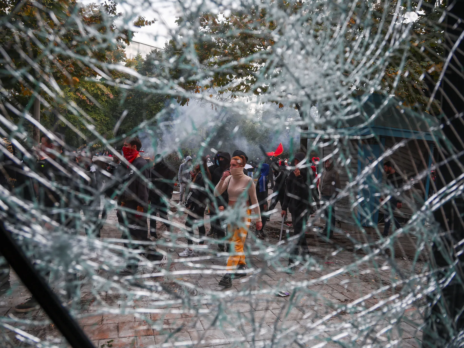 Demonstrator, seen through broken glass, gather during clashes with police amid an anti-government protest by students, in Tirana, Albania, October 15, 2026. REUTERS/Florion Goga