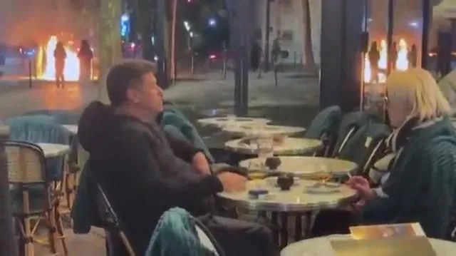Muškarac i žena uživali u piću i cigareti dok u pozadini Pariz "gori"